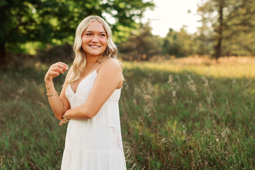 Natural light senior portrait of a high school senior standing in a grassy field with soft depth of field