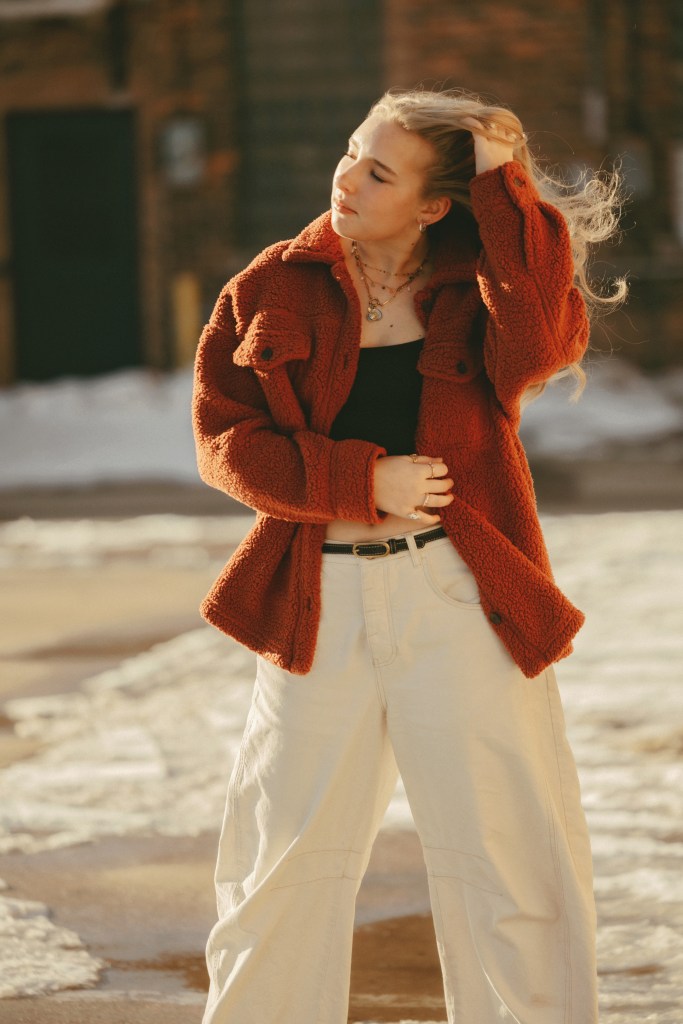 Senior photo of Aili in downtown St. Joseph, Michigan standing near a brick wall on a bright winter day, captured by a Southwest Michigan senior photographer.