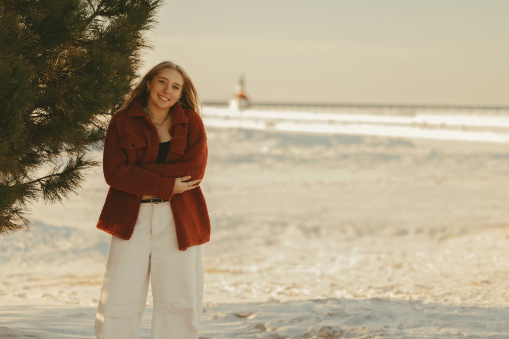 High school senior portrait of Aili at Silver Beach in St. Joseph, Michigan with golden winter sunlight reflecting off Lake Michigan behind her.
