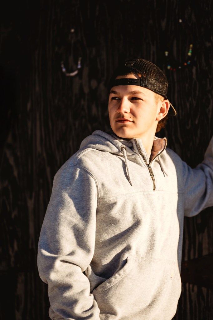 Senior portrait session male senior leaning on barn in winter golden hour southwest michigan