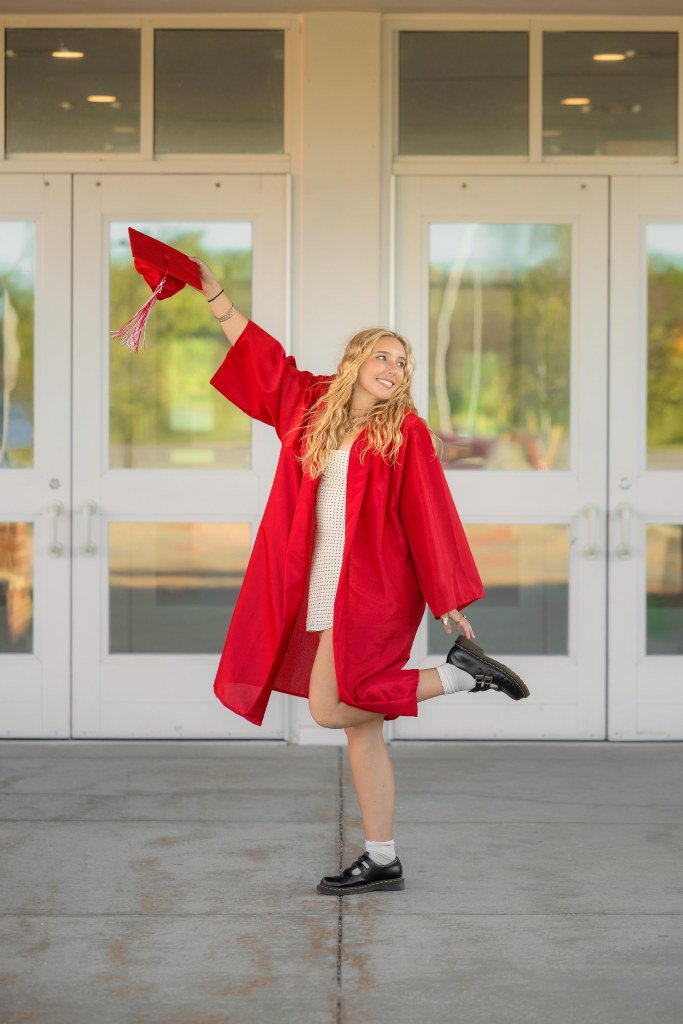 Senior holding cap wearing gown in front of Paw Paw high School in Paw Paw, mI
