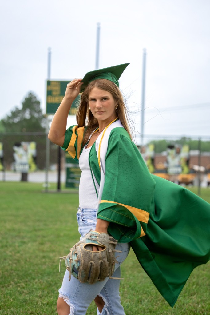 Coloma Varsity Softball senior posing in cap and gown on home softball field before graduation