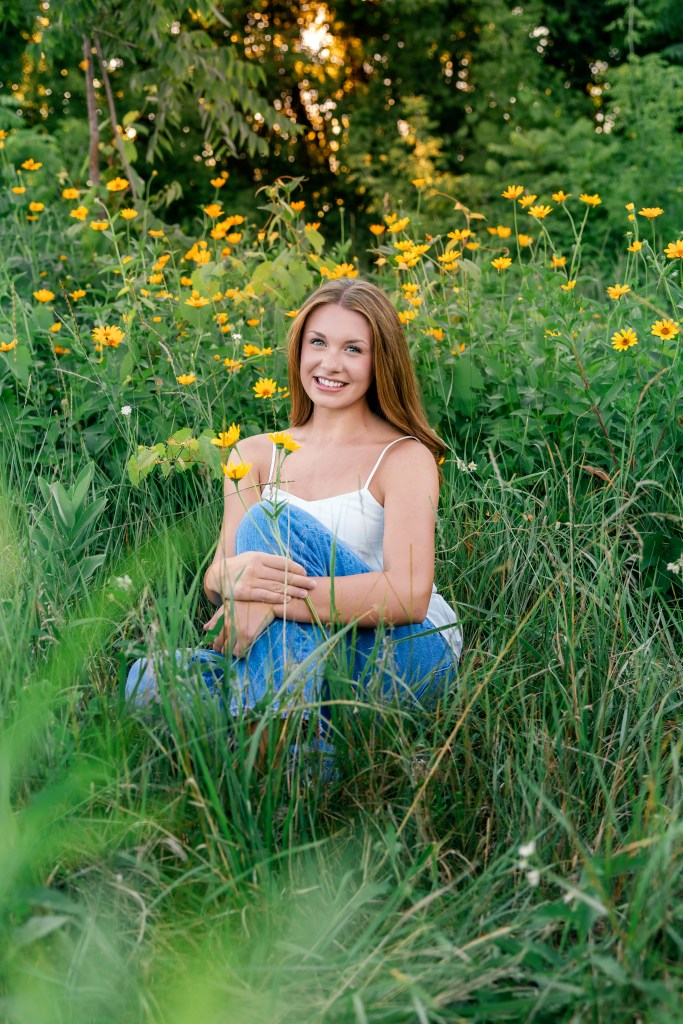 Emma sitting among native wildflowers and prairie grasses during her Southwest Michigan Class of 2027 senior photo session.