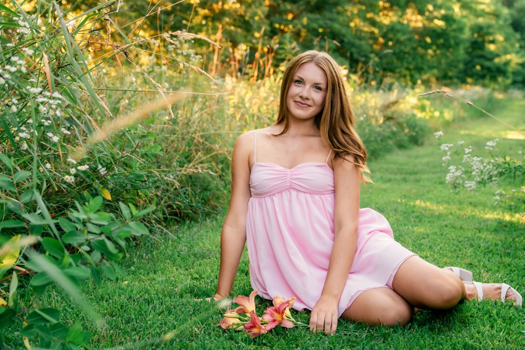 Senior portrait of Emma smiling in a blush pink dress surrounded by colorful wildflowers in Southwest Michigan.