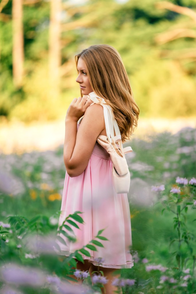 Emma carrying her very first pair of pointe shoes through a blooming wildflower field during her Class of 2027 senior session.