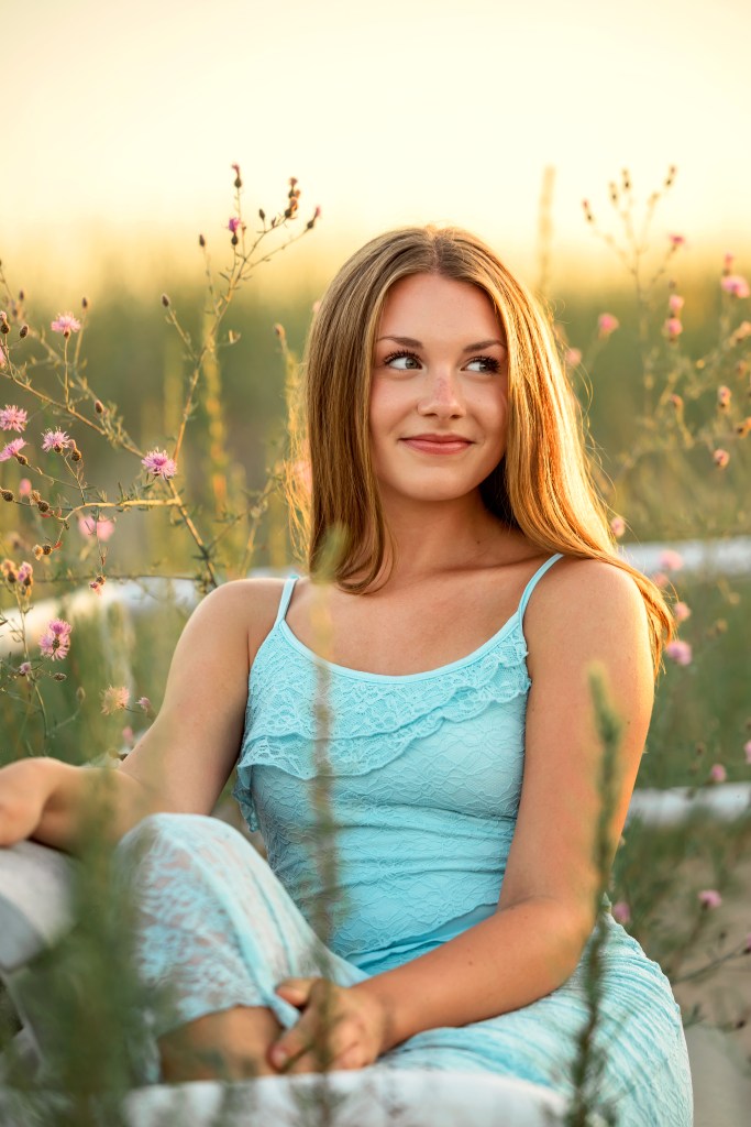 St. Joseph High School senior Emma sitting among blooming beach wildflowers at Jean Klock Beach during her Class of 2027 senior photo session.