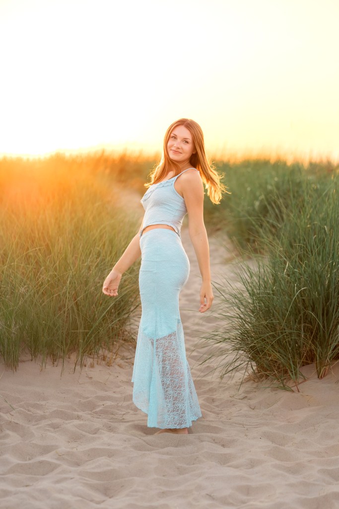 Golden hour portrait of Emma surrounded by dune grass at Jean Klock Beach, with warm Lake Michigan sunset light during her St. Joseph High School senior pictures.