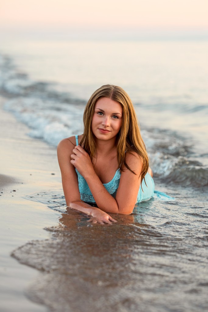 St. Joseph High School senior Emma posing along the shoreline at Jean Klock Beach with warm golden hour light reflecting off Lake Michigan.