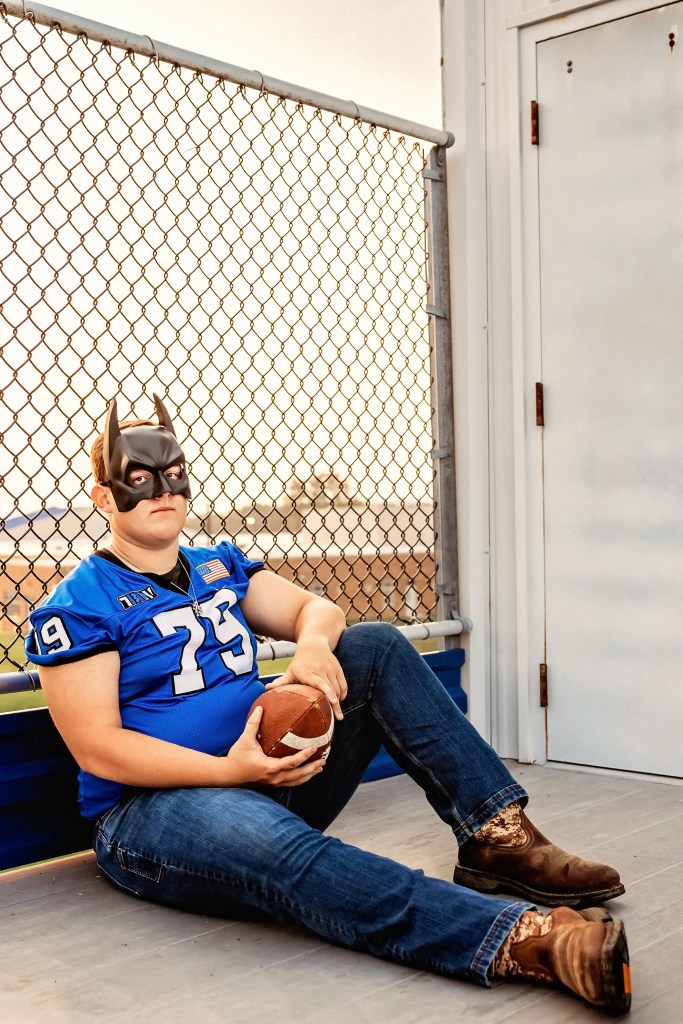 Lawton High School Class of 2027 senior holding a football while sitting against a chain-link fence at Lawton High School.