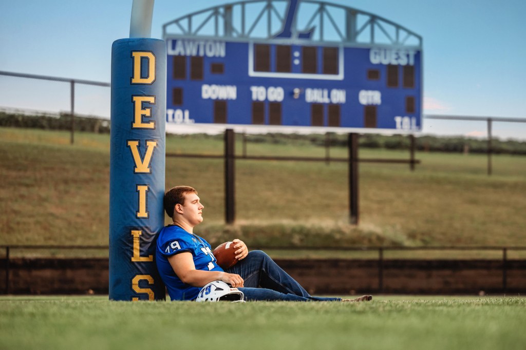 Lawton High School Class of 2027 senior leaning on the football stadium railing during golden hour.