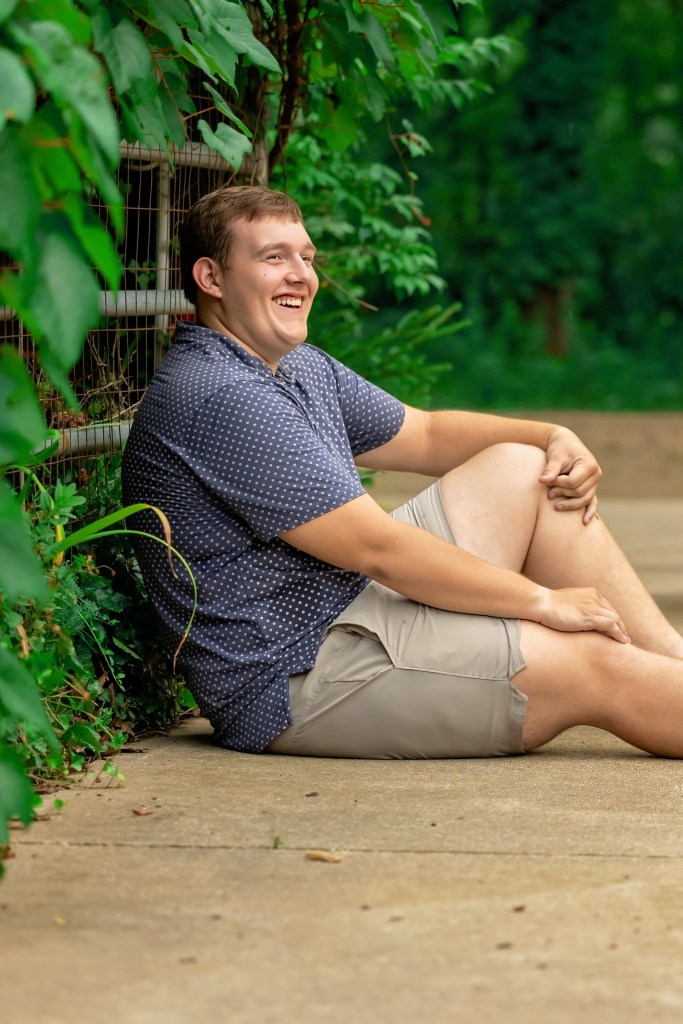 Lawton High School Class of 2027 senior sitting on a wooded path at his grandfather's property during a Southwest Michigan senior portrait session.