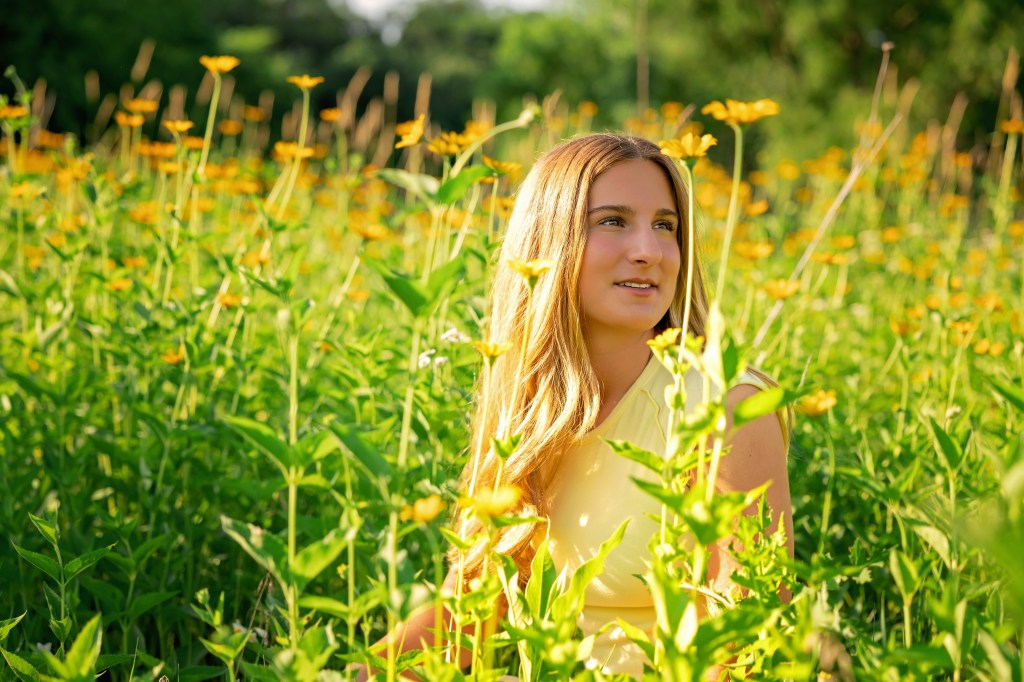 High school senior in a yellow top and white skirt surrounded by Michigan summer wildflowers.